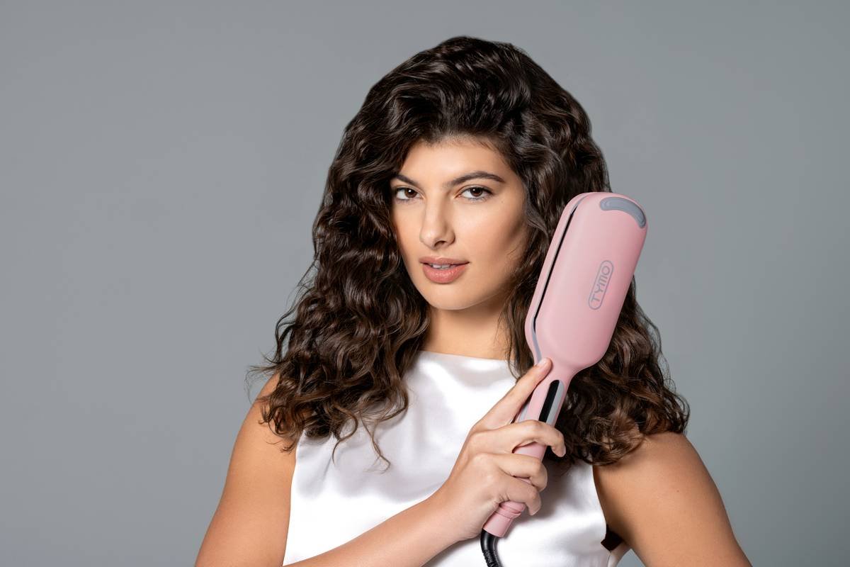 A woman with cascading curls holds a TYMO hair styling tool, merging style and technology to craft her unique, bold look.