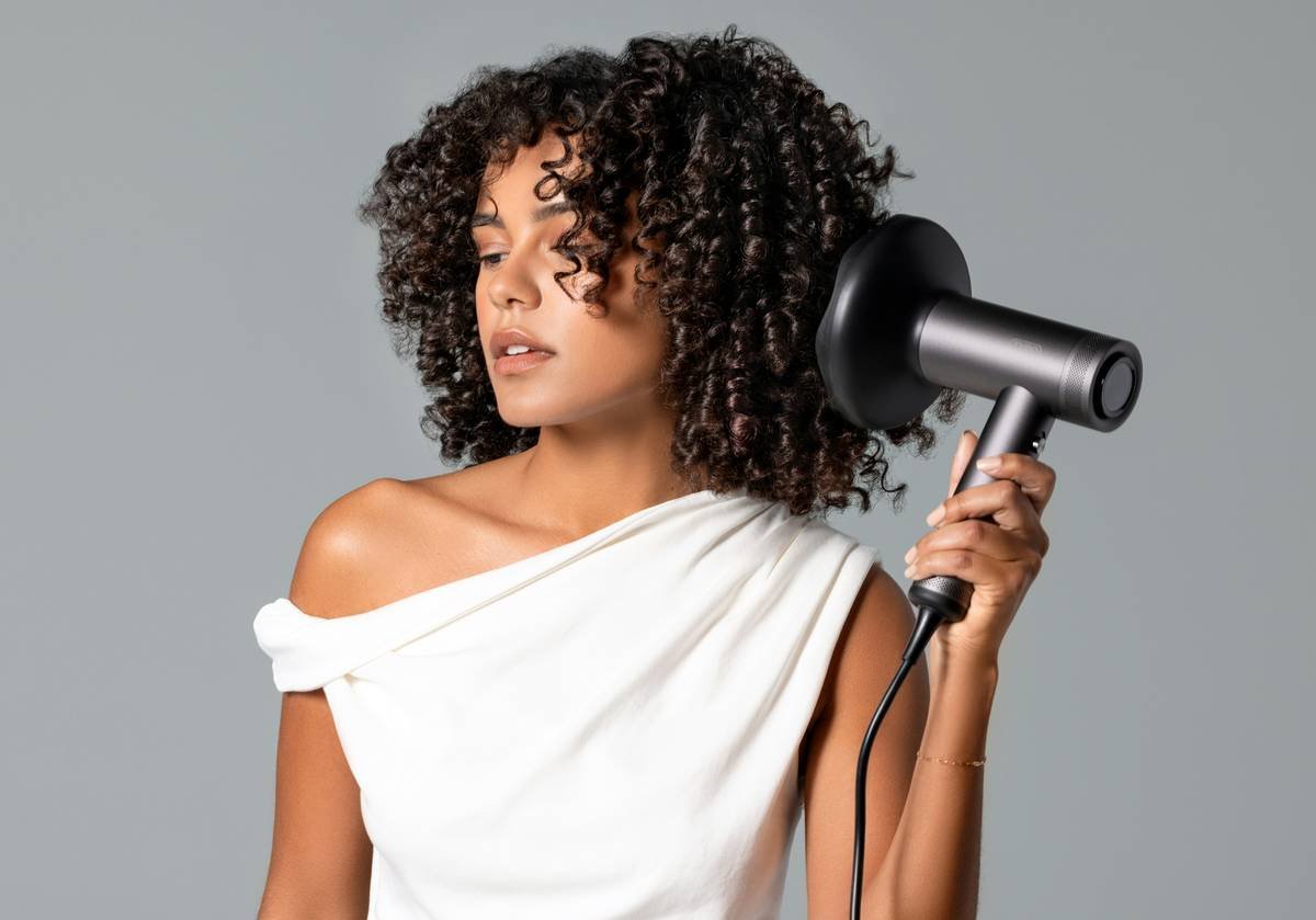 Woman demonstrating twist curl technique on damp hair using satin-covered rollers